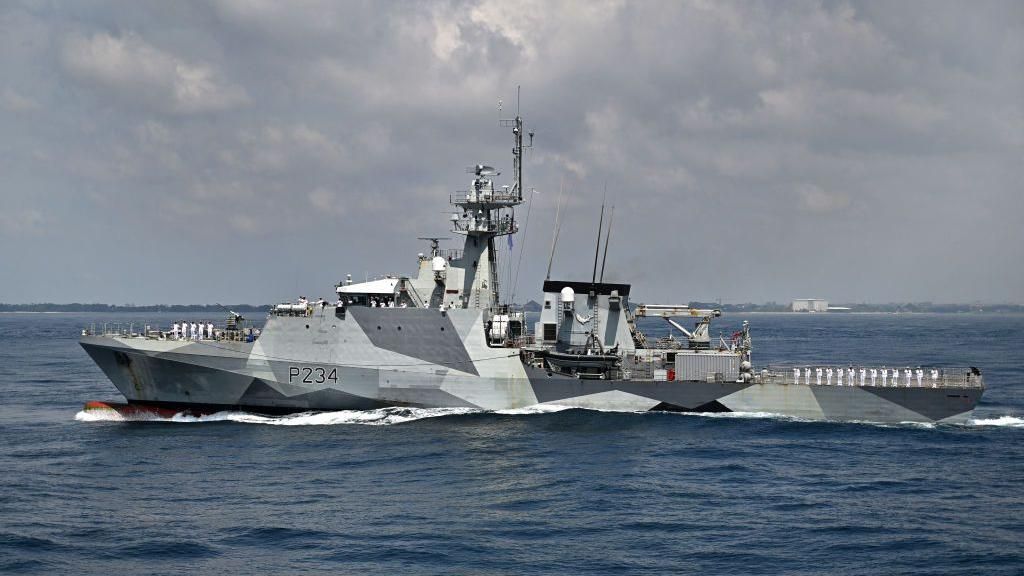 Wide shot of HMS Spey, a large grey vessel, in the sea.
