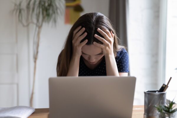 Frustrated unhappy laptop user girl touching head at work table with computer