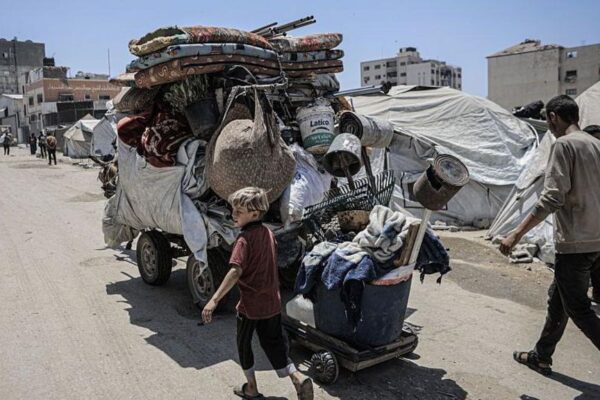 A young boy and adult man walk alongside a large trailer filled with belongings in Gaza City. A horse is pulling the large trailer