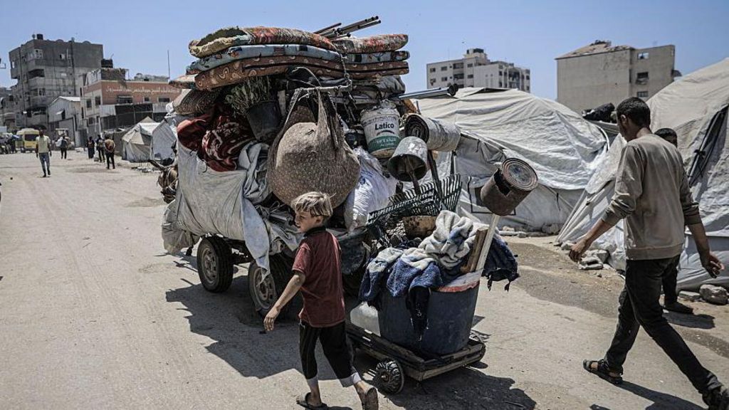 A young boy and adult man walk alongside a large trailer filled with belongings in Gaza City. A horse is pulling the large trailer