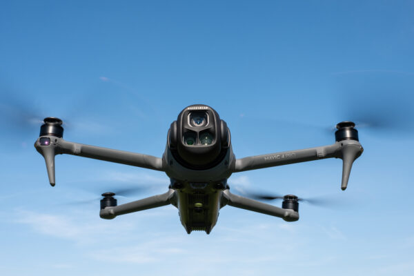 DJI Mavic 4 Pro in flight against a blue sky facing towards the camera with the drone camera and gimbal visible