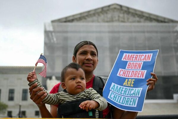 A mother with her infant son hold a US flag and sign saying
