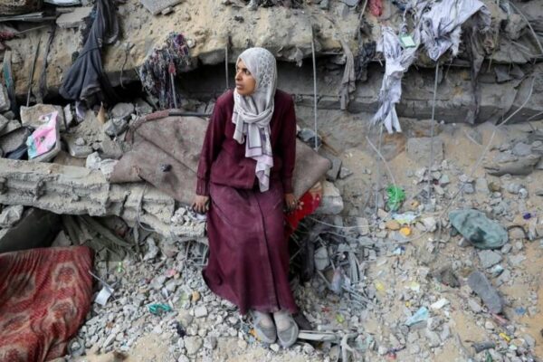 A Palestinian woman looks to her right, sitting amidst the rubble of a very badly damaged building in Gaza City